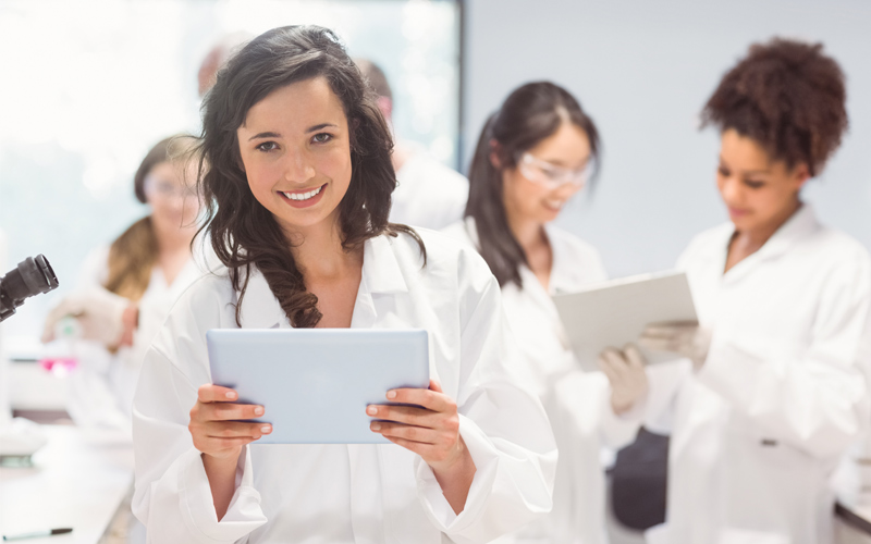 Woman in labcoat holding tablet and smiling at camera