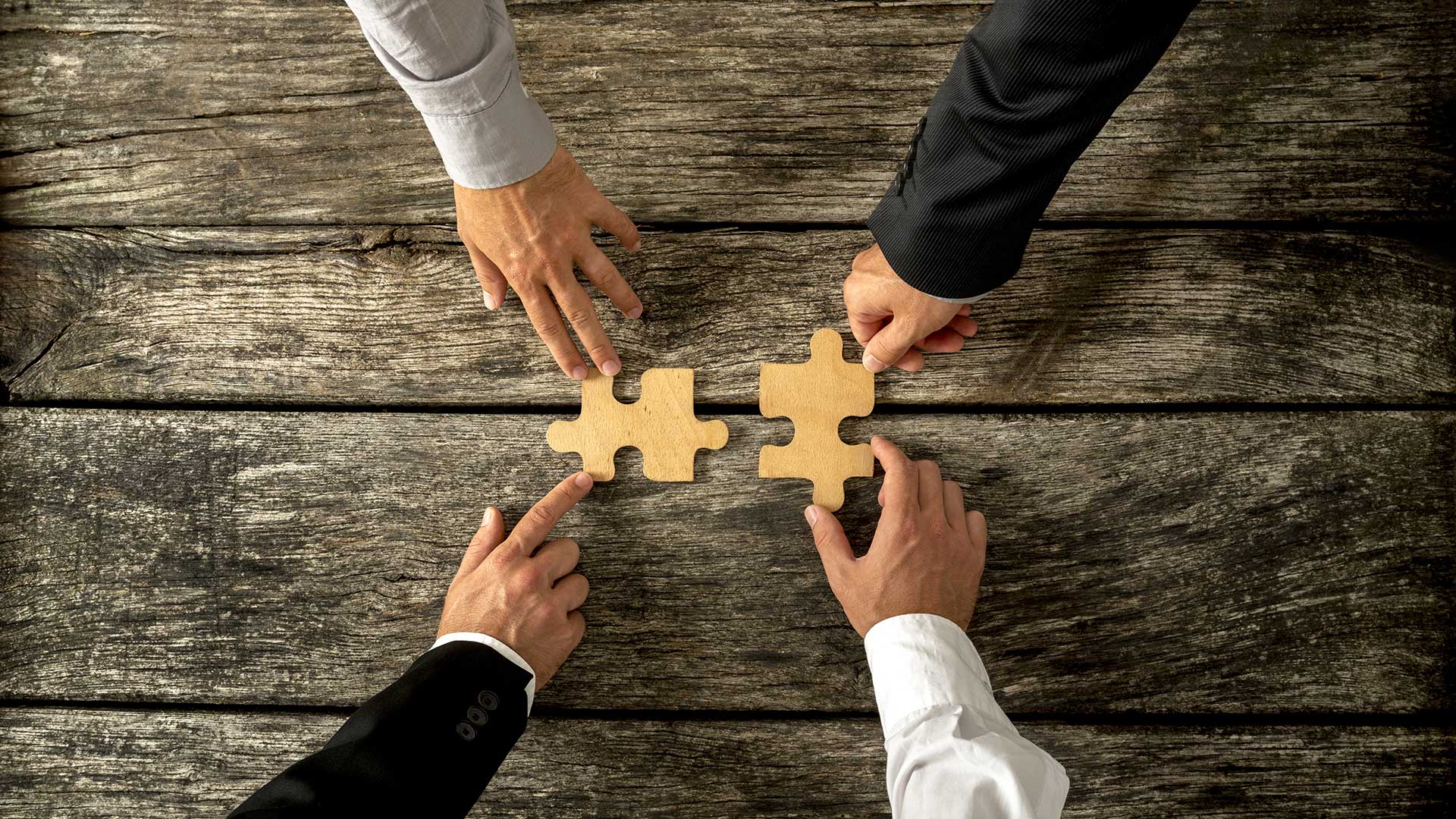 Overhead shot of four people putting two puzzle pieces together